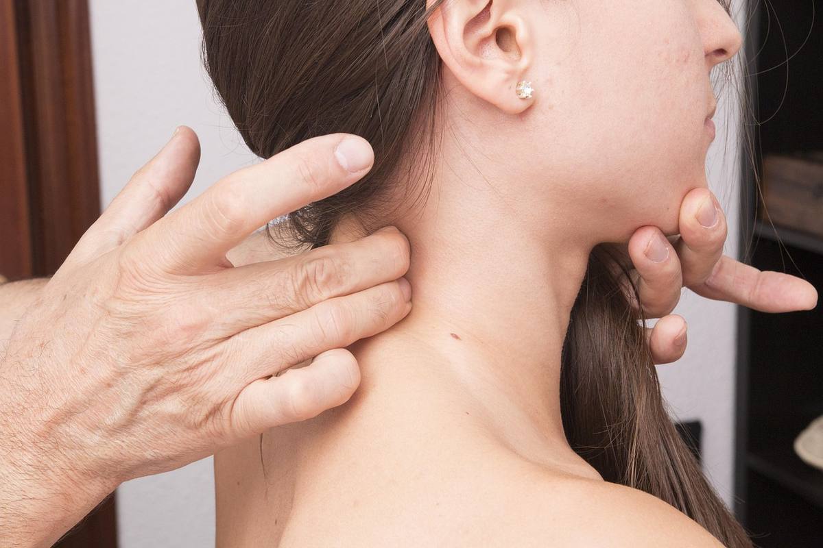 Une main masse le cou d'une femme, son oreille et un petit earring visibles