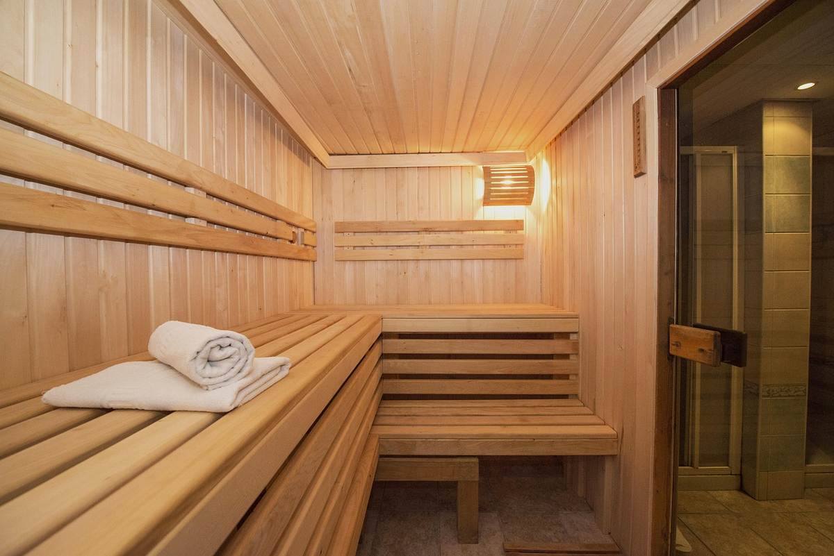 Sauna en bois avec banquettes étagées, serviette blanche et porte vitrée
