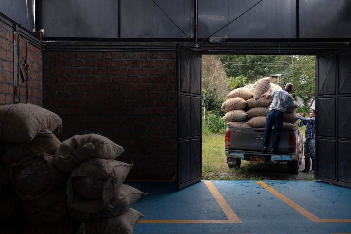 Des sacs dans un hangar, un camion chargé de sacs, deux personnes en train de décharger Des sacs dans un hangar, un camion chargé de sacs, deux personnes en train de décharger